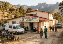 Rural health clinic building in Mexico with people sitting and walking nearby and an ambulance parked outside