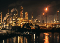 Oil refinery complex with tall smokestacks and flames burning at night
